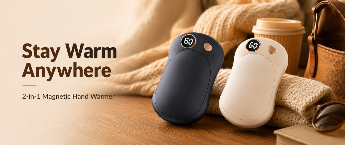 Two magnetic hand warmers, one dark navy blue and one cream white, displayed on a wooden table next to a cozy knitted sweater, coffee cup, and sunglasses. Text on the left reads 'Stay Warm Anywhere' and '2-in-1 Magnetic Hand Warmer'.